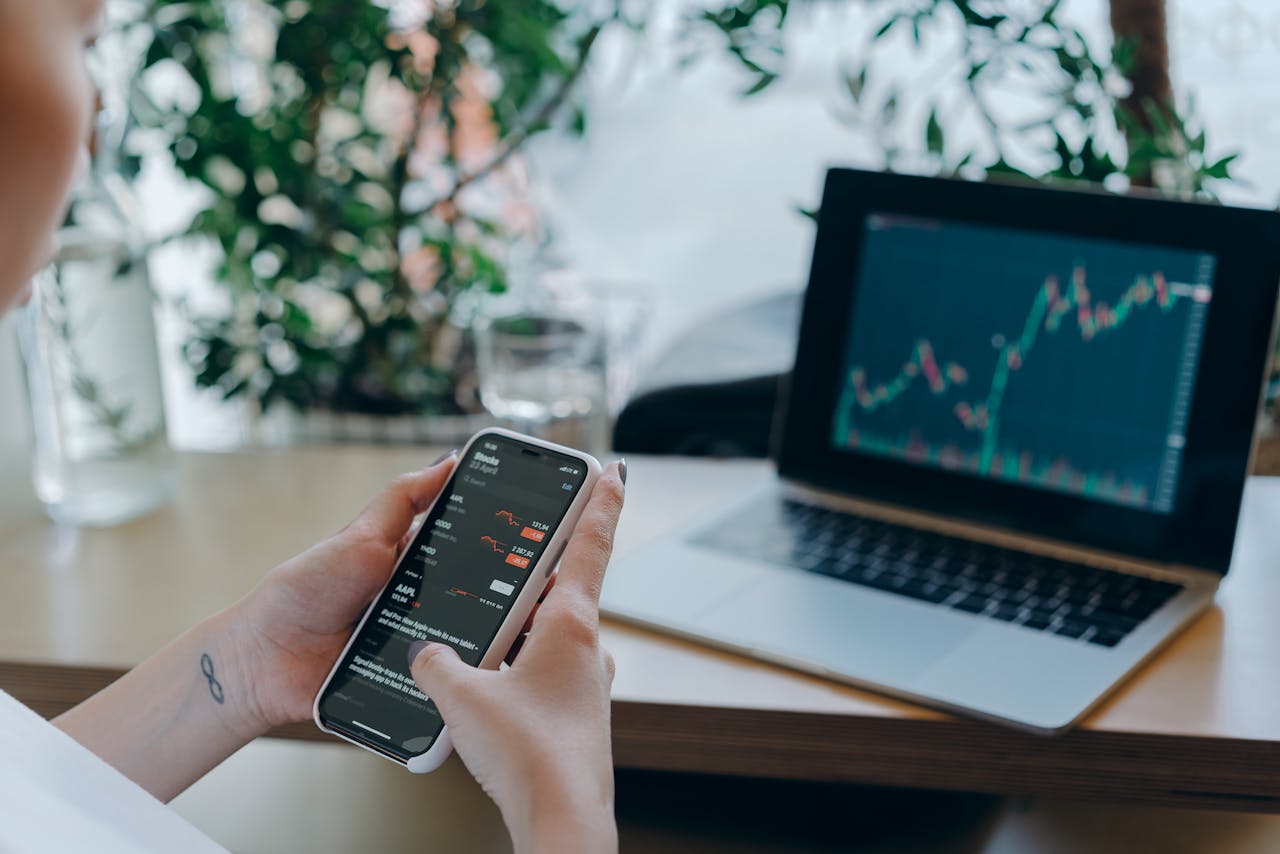 Cryptocurrency trading dashboard on a laptop screen, with a mobile phone showing price alerts.